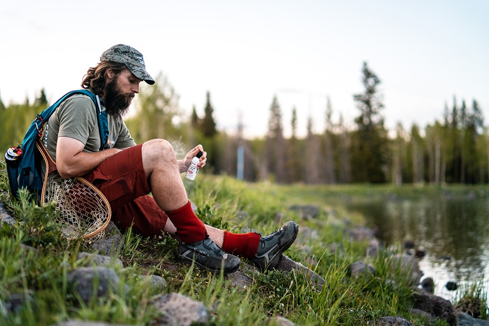 A white male hiker sitting by the lake holds a Tecnu Calagel after touching a poison ivy.