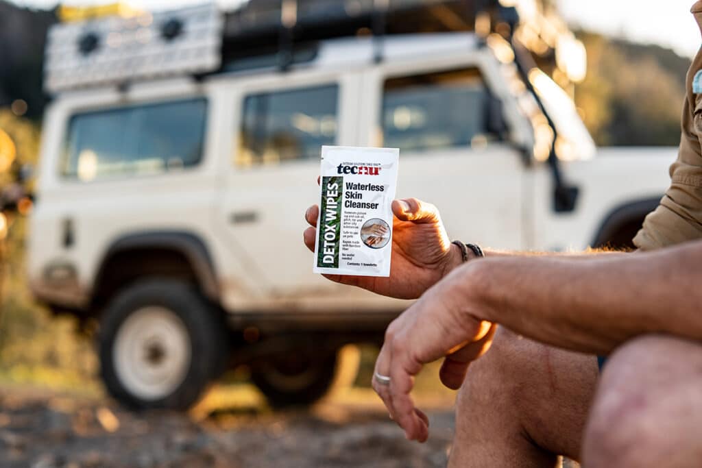 An outdoorsman is holding a Tecnu Detox Wipes while sitting in the open.