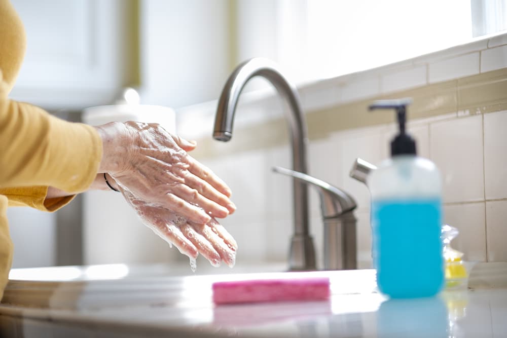 A woman washing her hands at the kitchen sink for sanitation.